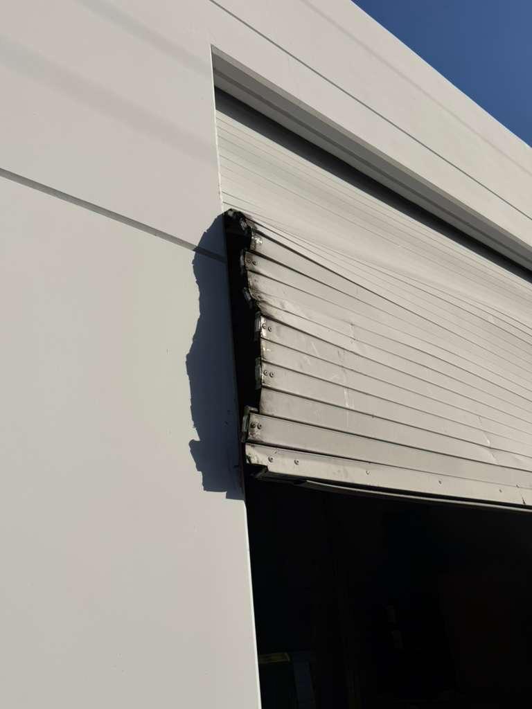 Commercial roll-up garage door slat damage close-up showing bent and misaligned panels before repair