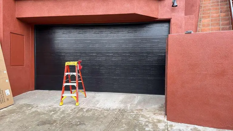 Solid black modern garage door with textured horizontal panel design installed on residential red brick property in Los Angeles